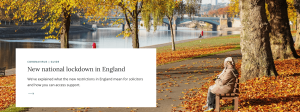 An elderly person sits on a bench in a park with autumn leaves, near a river. There's a notice about a new national lockdown in England on the left side of the image.