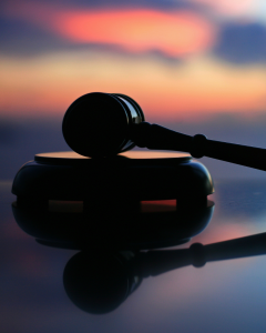 A judge’s gavel and sound block are silhouetted against a blurred, colorful sunset background.