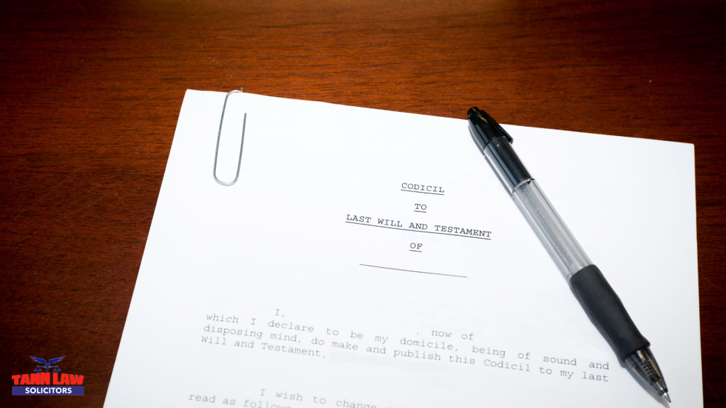 Here's some alt text for the image:
Descriptive (for accessibility):
"A printed codicil to a Last Will and Testament document resting on a wooden desk, with a pen and paperclip placed on top.